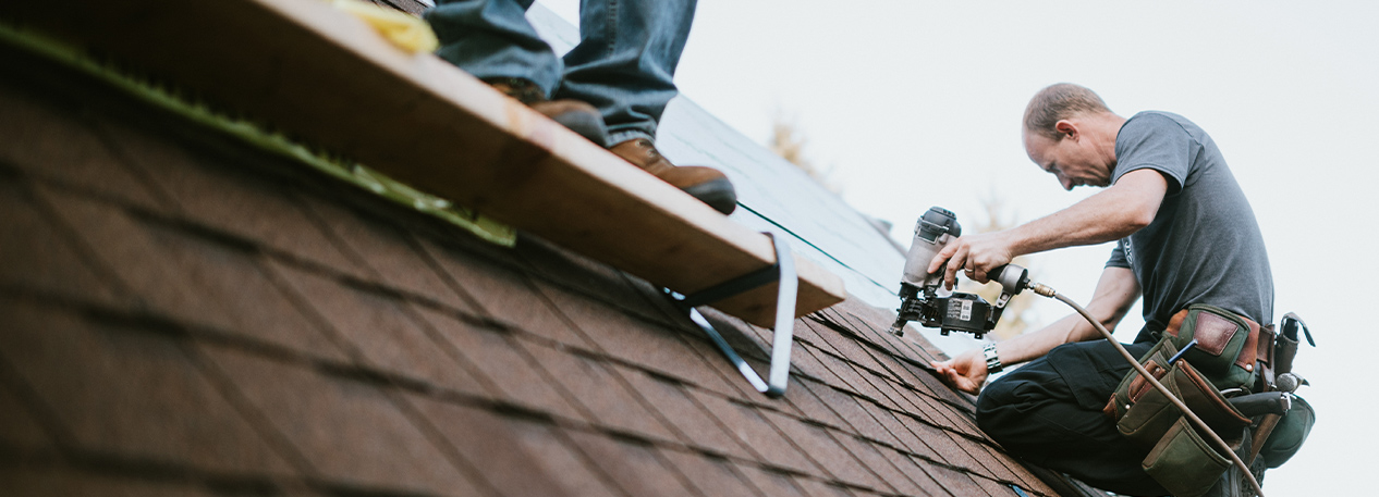 Roofers use tools to fix shingles on a roof.