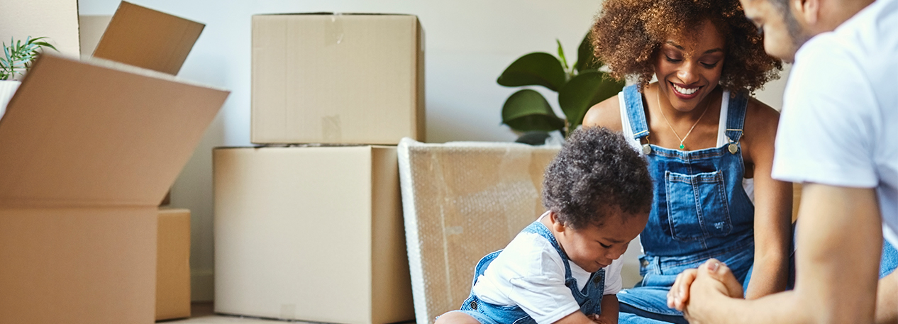 A young family enjoy each other's company while they sit on the floor surrounded by moving boxes.