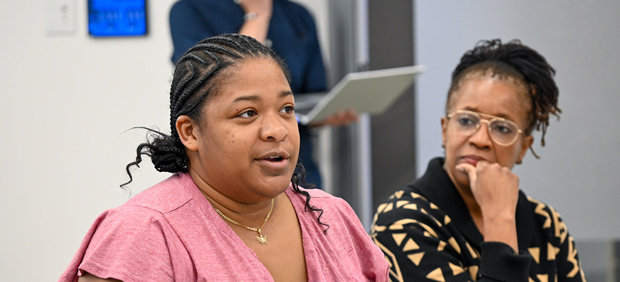 A woman speaking at a work event, with another woman looking on intently.