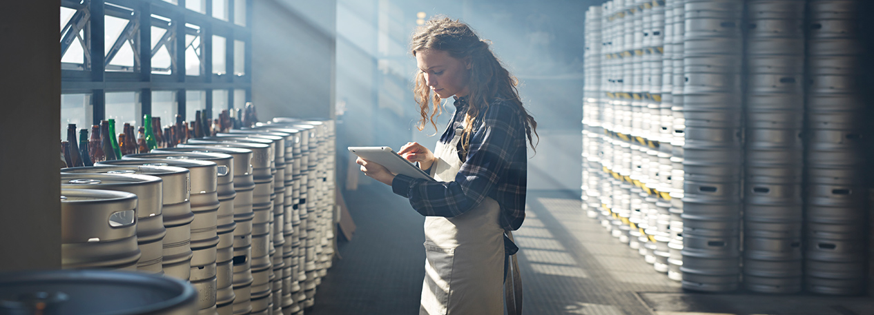 Woman with a tablet computer in a warehouse with stacks of beer kegs