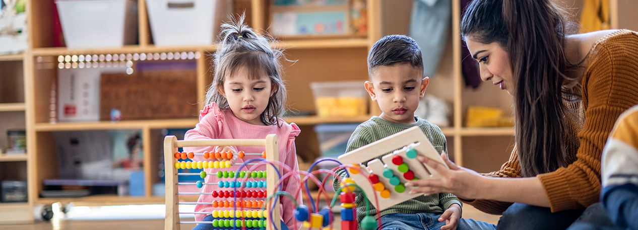 Two young children, guided by their teacher, play with colorful toys.