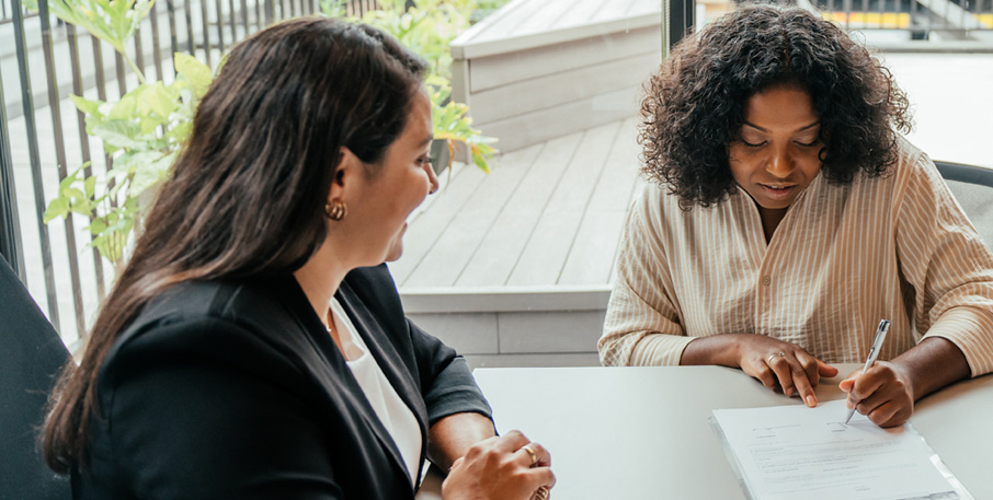 A woman signs a document as a banker looks on.