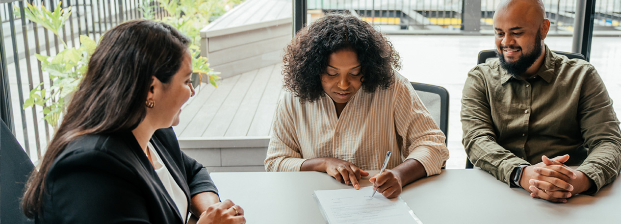 A woman signs a document as a banker looks on.