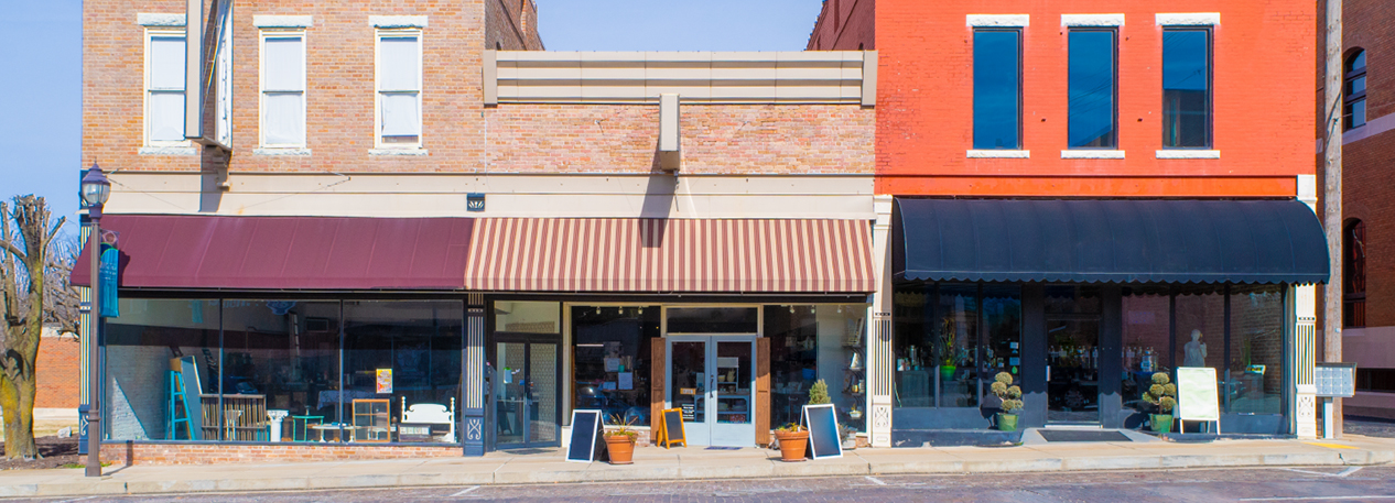 A row of three storefronts with awnings and promotional signs on the sidewalk