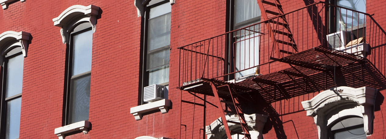 Close-up of red brick building with windows and red, metal fire escape
