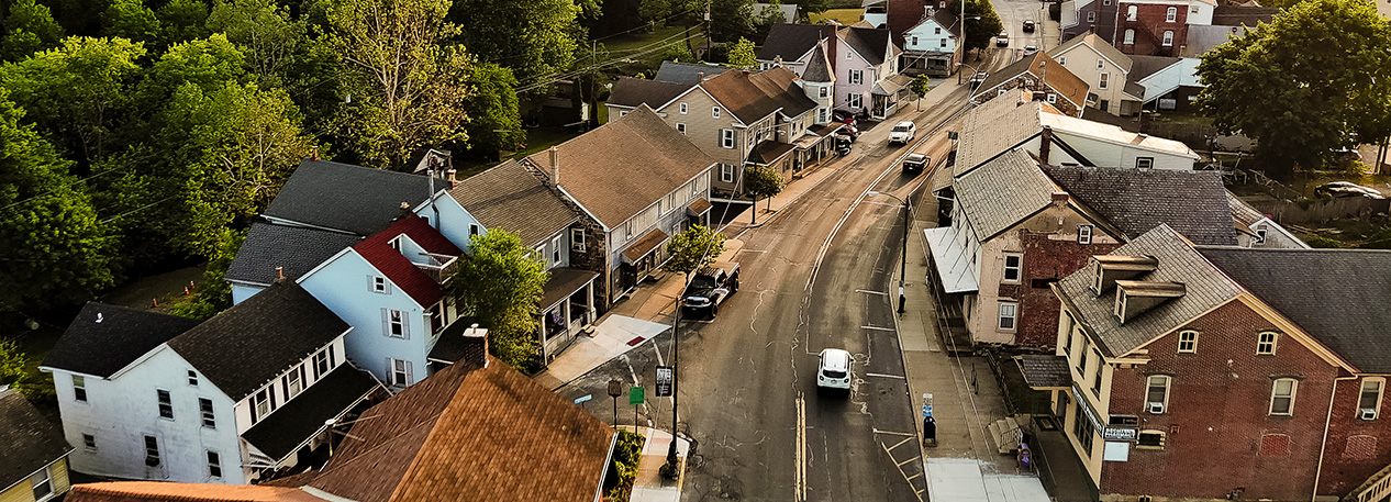 Cars driving down a road lined with homes in a small rural town.