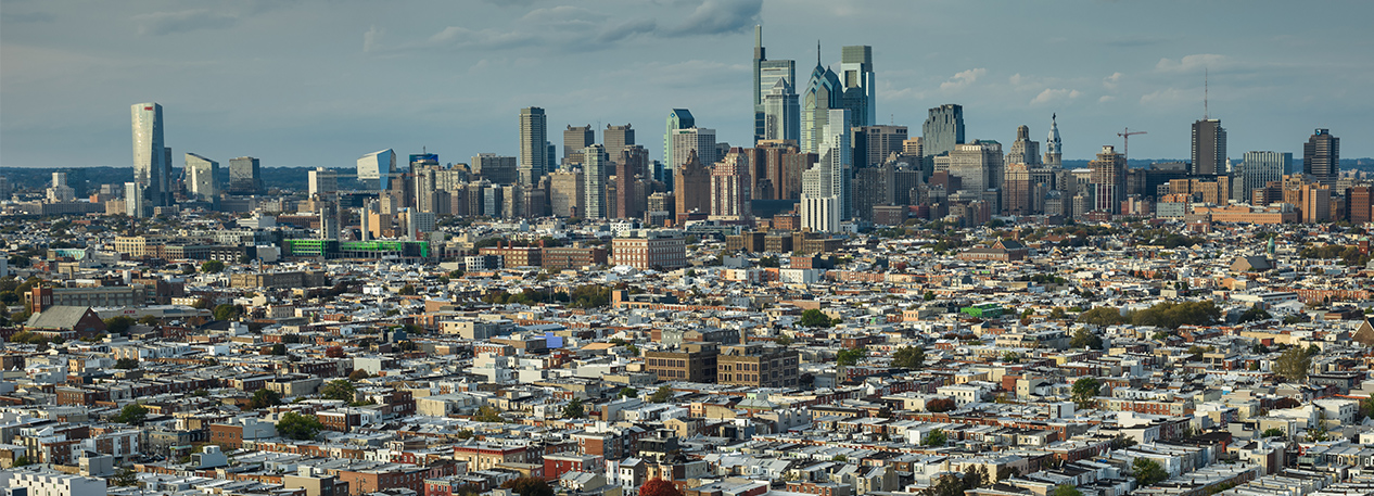 Tall buildings loom in the distance and are surrounded by many blocks of row homes in the city of Philadelphia, PA.