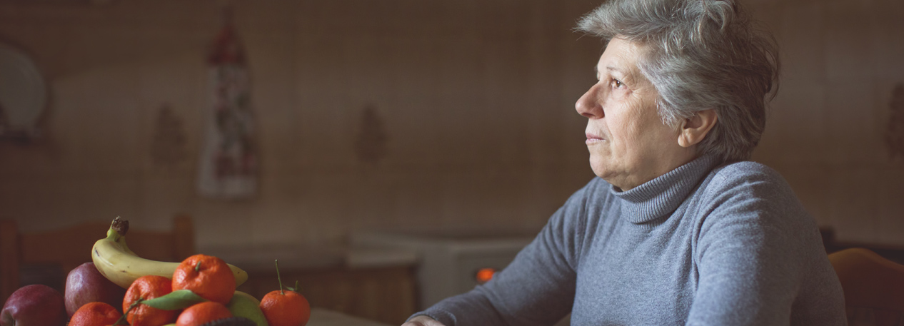 Woman sitting at a kitchen counter with a bowl of fruit in front of her.