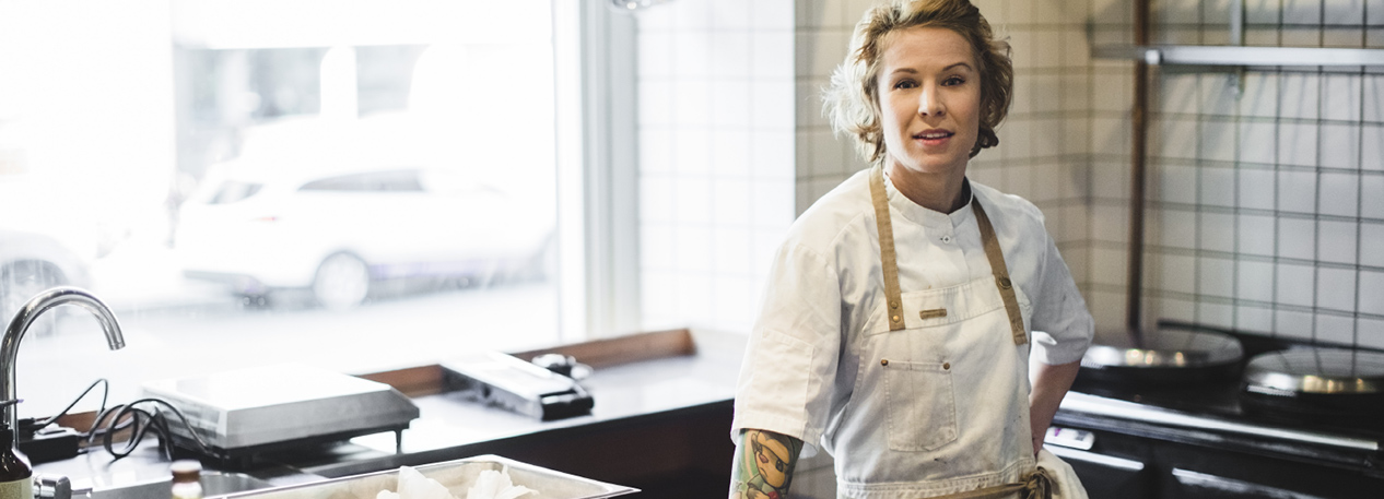 Woman in white jacket and apron standing in a restaurant kitchen