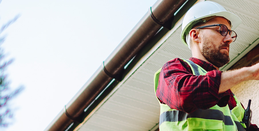 Man on a ladder in a hard hat working on a house