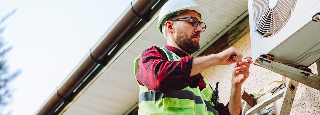 Man on a ladder in a hard hat working on a house