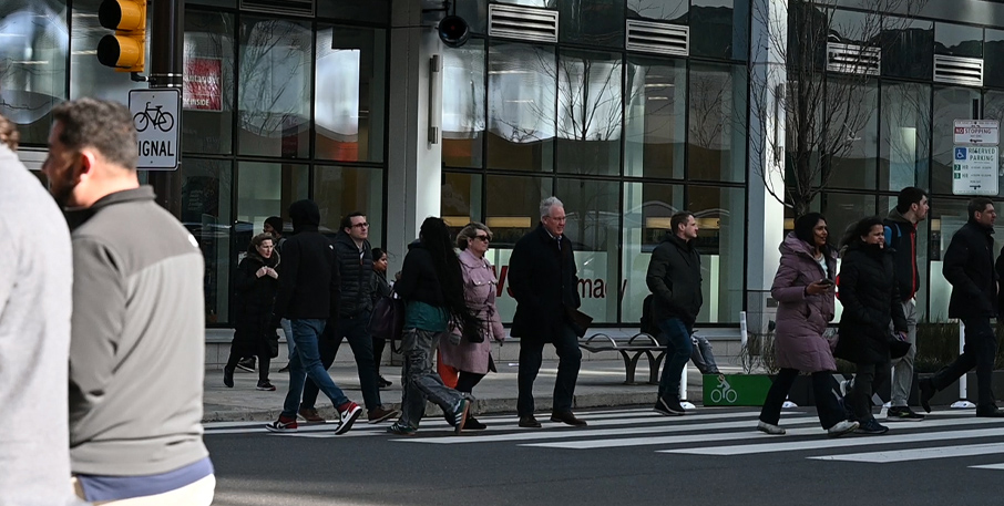 A crowd of people walking across the street in a crosswalk in the middle of a city.