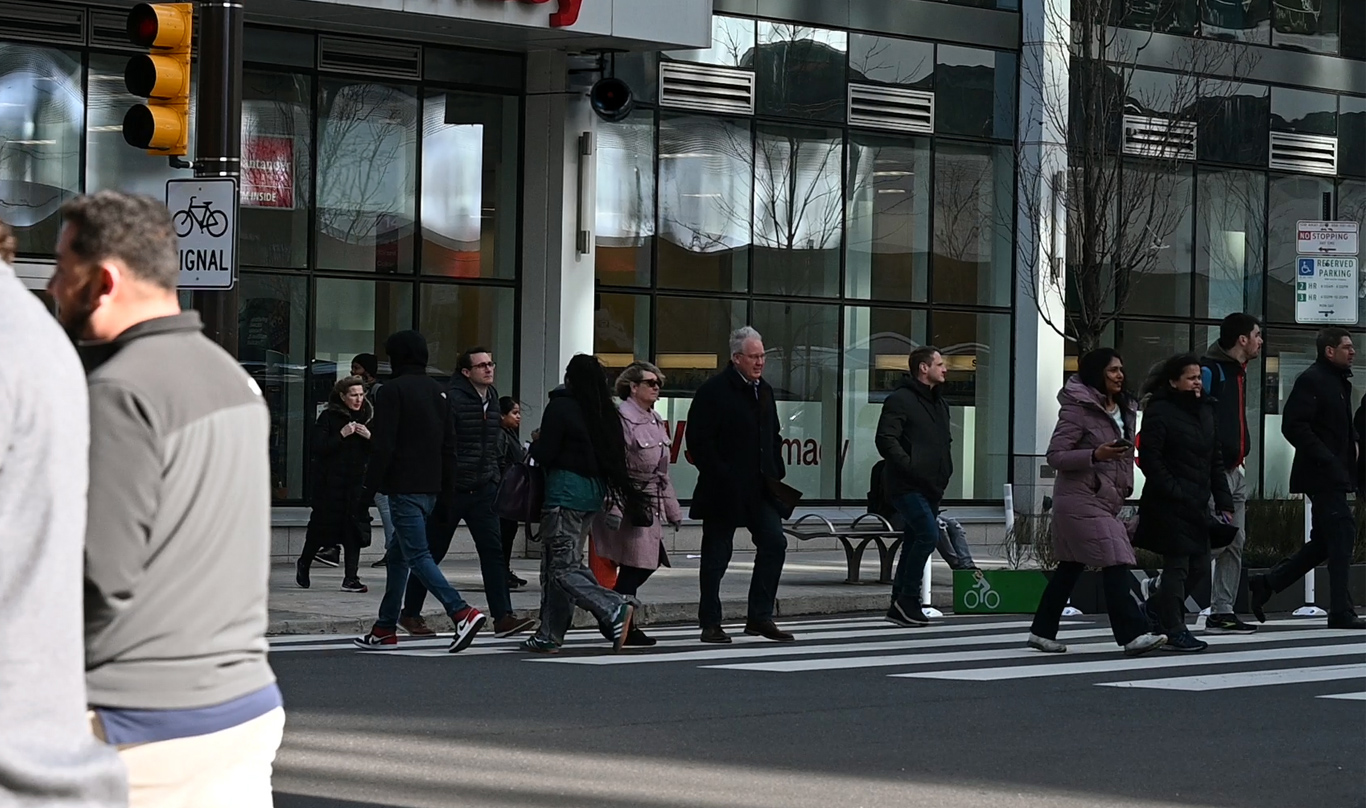 A crowd of people walking across the street in a crosswalk in the middle of a city.