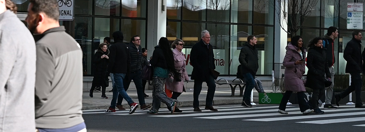 A crowd of people walking across the street in a crosswalk in the middle of a city.