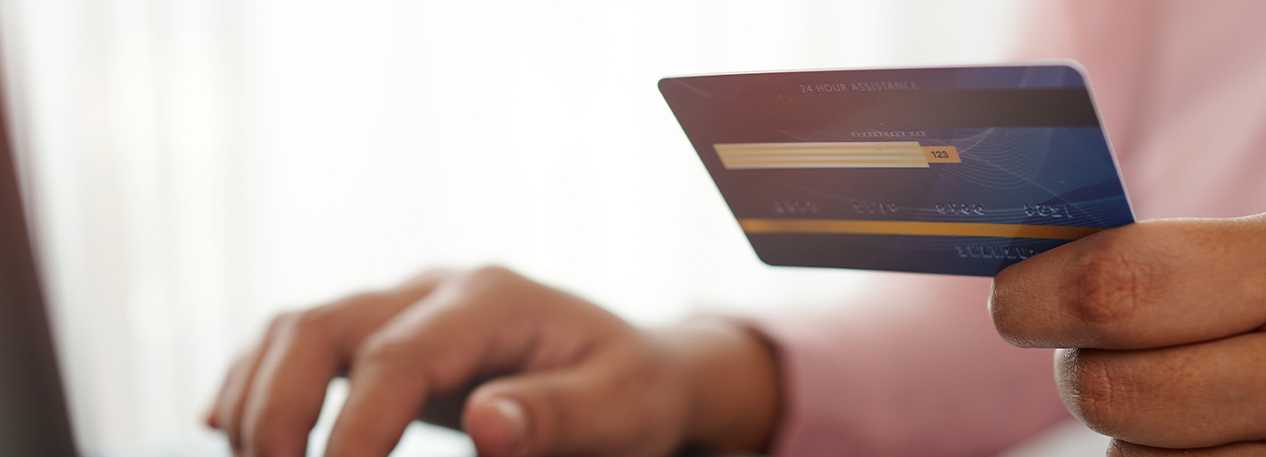 A person types at a laptop computer while holding a credit card.