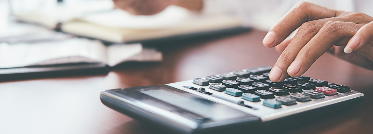 A person sitting at a desk with an open notebook, entering numbers in to a calculator.