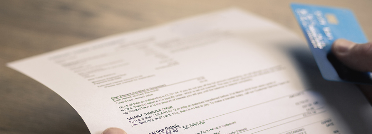 A close-up image of hands holding a bill and a credit card.