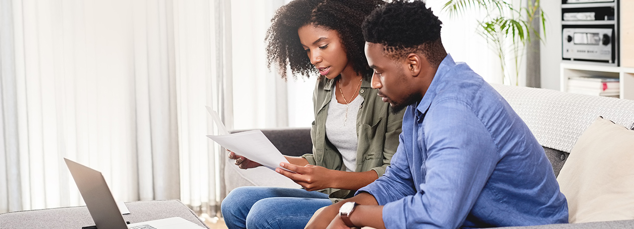 Couple on couch, sitting in front of a laptop computer, looking at papers