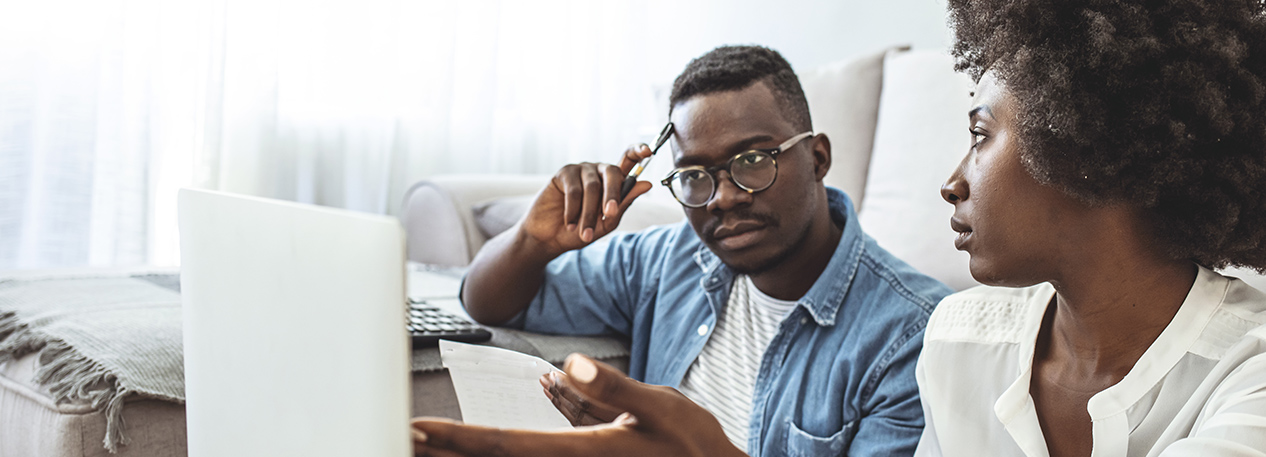A Black couple looks stressed out as they view bills on their laptop.