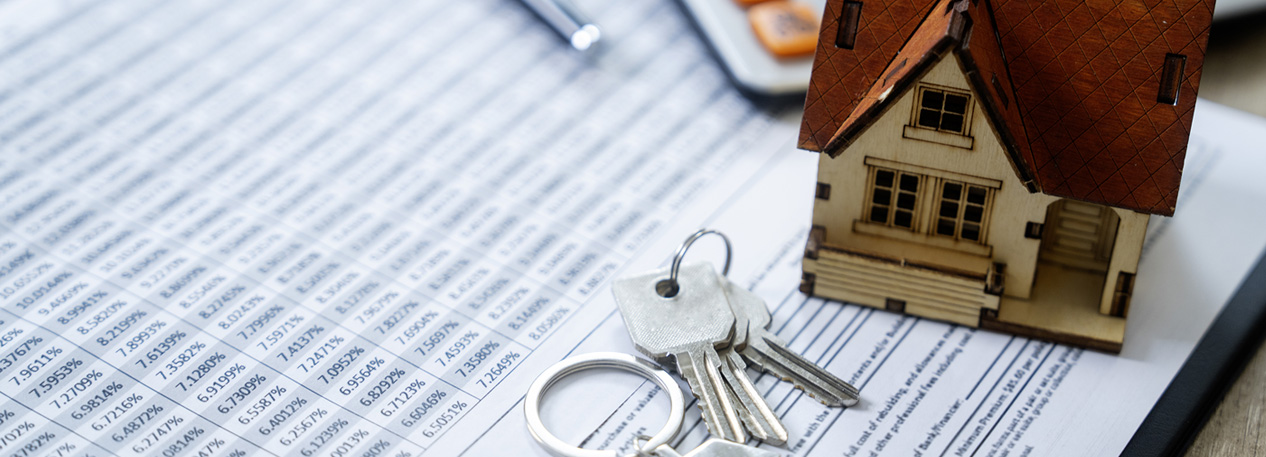 A set of keys and a figurine of a house sit on top of mortgage paperwork.