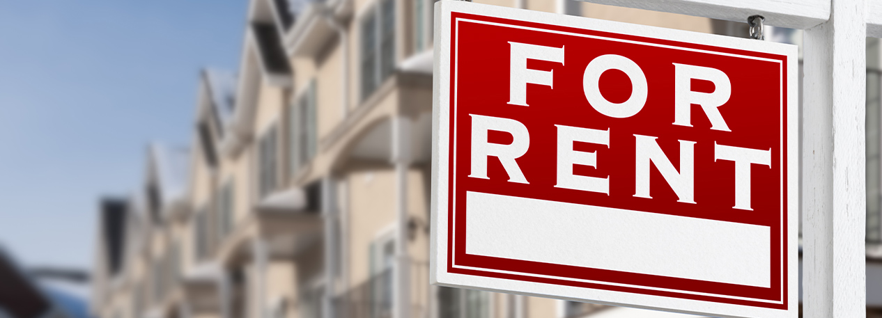 A For Rent sign in the foreground and an apartment building in the background.