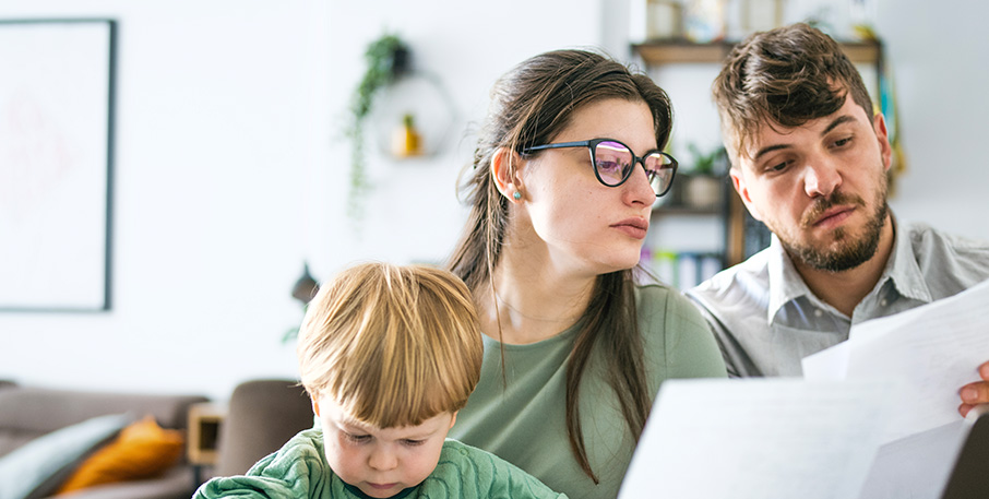 Two parents read bills together while their young son plays.