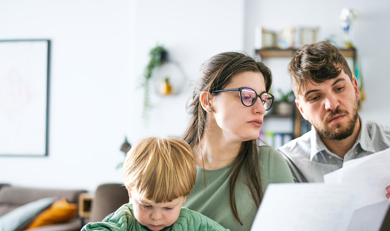 Two parents read bills together while their young son plays.