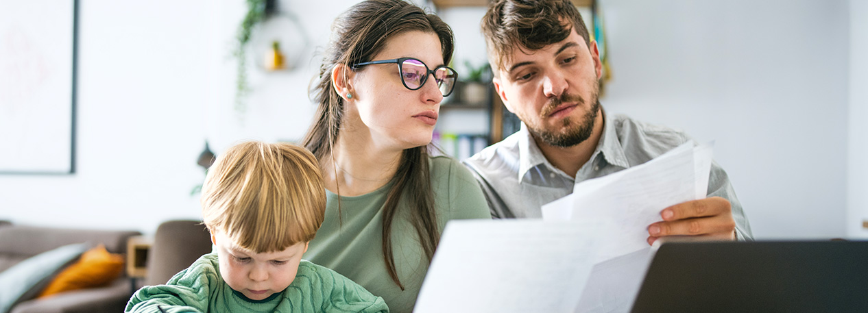 Two parents read bills together while their young son plays.