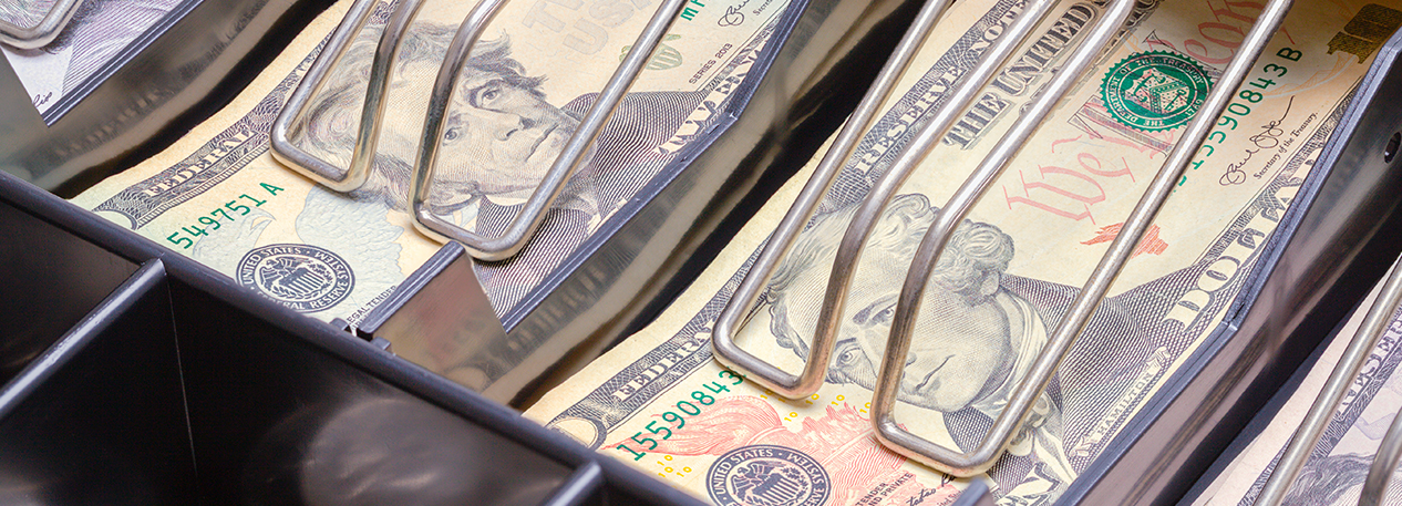 Open drawer of a cash register filled with ten- and twenty-dollar bills and quarters in a tray