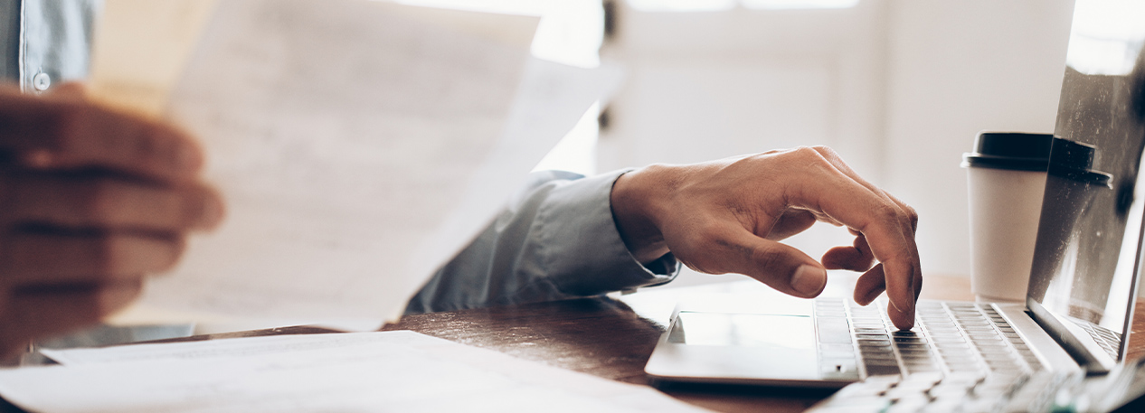 A man holds bills in one hand and types on a laptop with the other.