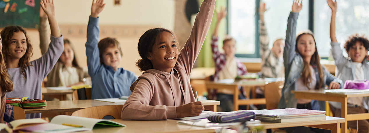 Young students in a classroom raising their hands