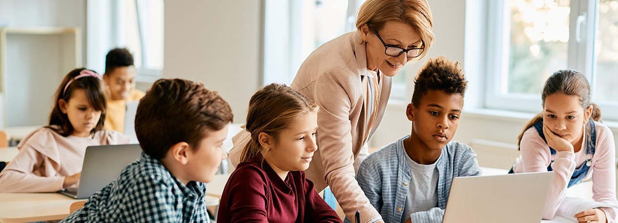 A teacher helps students at their desks.