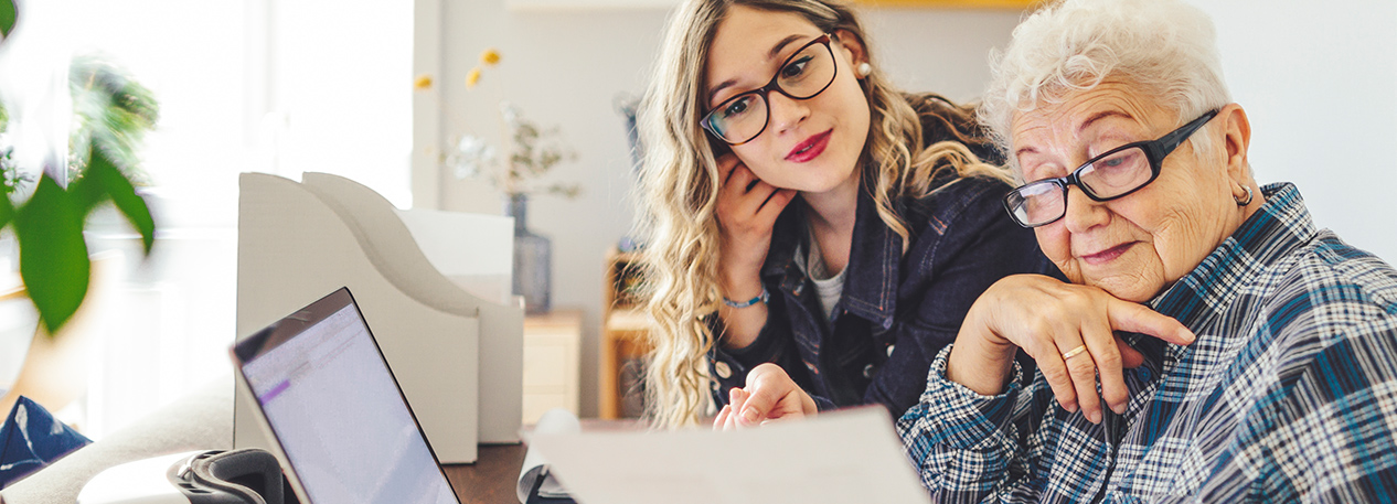 A senior woman reviews documents as her daughter looks over her shoulder.