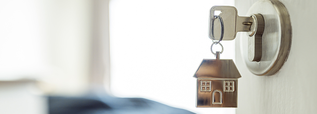 A key with a keychain in the shape of a house is in the lock of an open door.