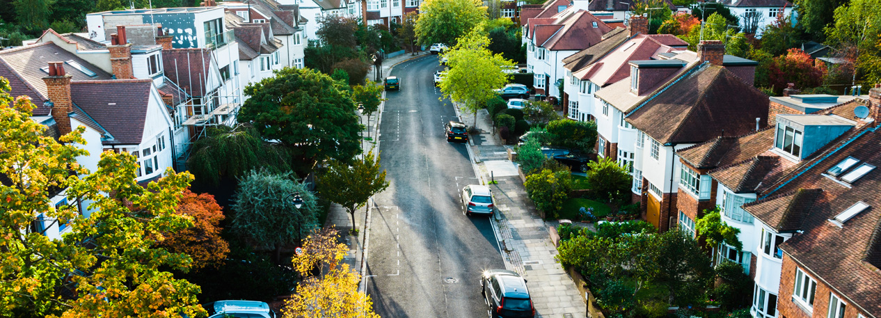 A tree-lined street with townhomes and cars on the road and parked in driveways.