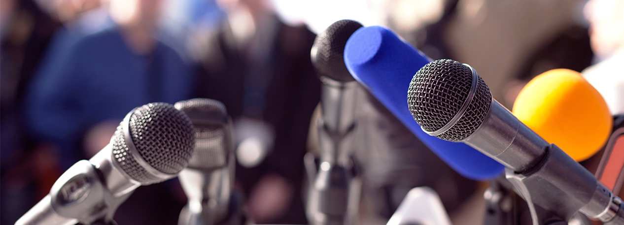 A variety of microphones sitting on a table with an audience in the distance