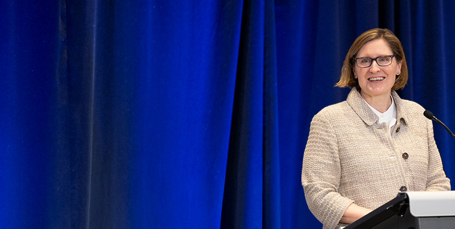 Anna Paulson stands at a podium in front of a blue curtain.