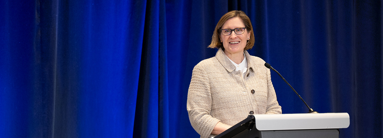Anna Paulson stands at a podium in front of a blue curtain.