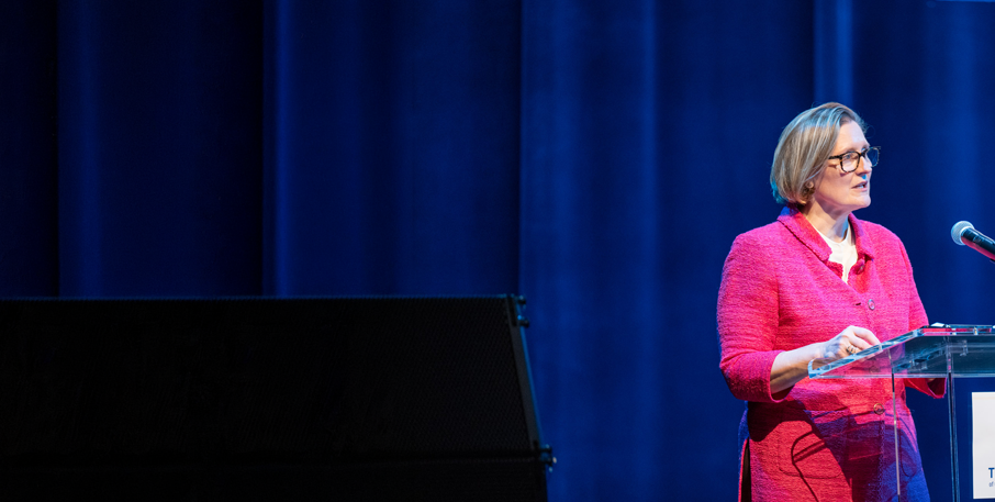 President Paulson speaks from a podium on a stage.