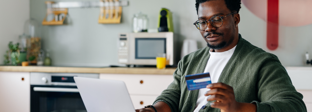 Man looking at credit card while using laptop
