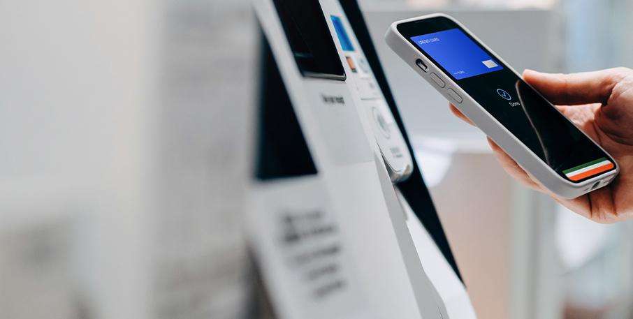 Image of a hand holding a phone displaying a digital wallet next to an ATM.