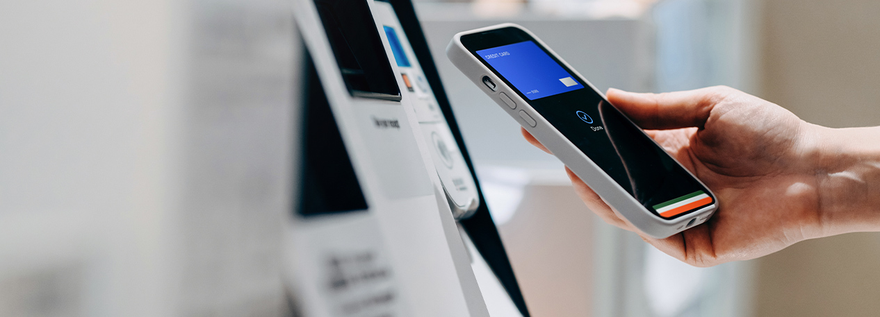 Image of a hand holding a phone displaying a digital wallet next to an ATM.