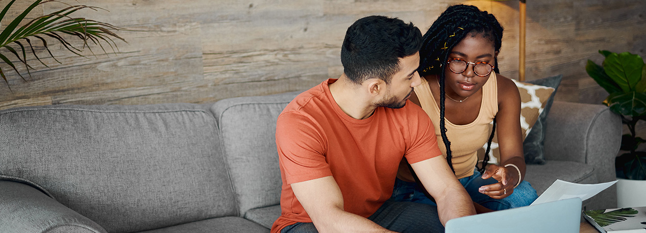Two people sitting on a couch, looking at a laptop together.