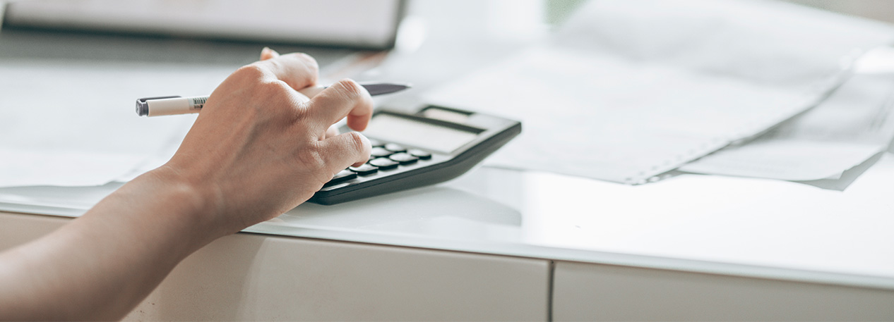 A woman fills out paperwork at a desk with a pen and calculator in hand.