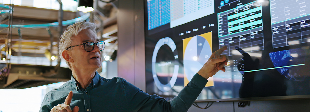 A lecturer stands in front of a data dashboard and gestures toward it.