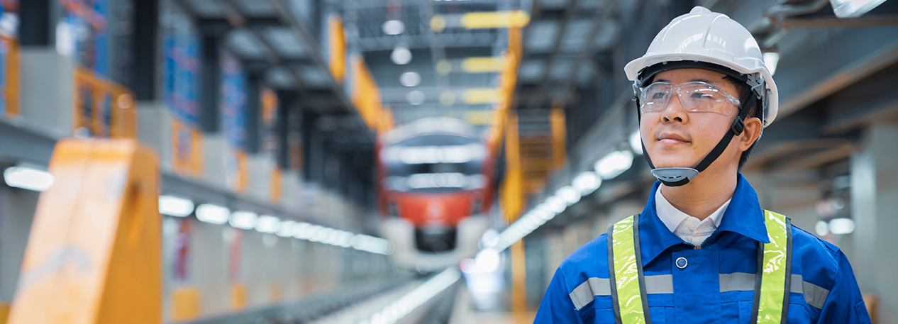 An engineer wearing a hardhat and safety goggles walks through a factory.