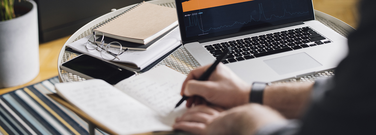 Someone writing next to a laptop displaying a line graph