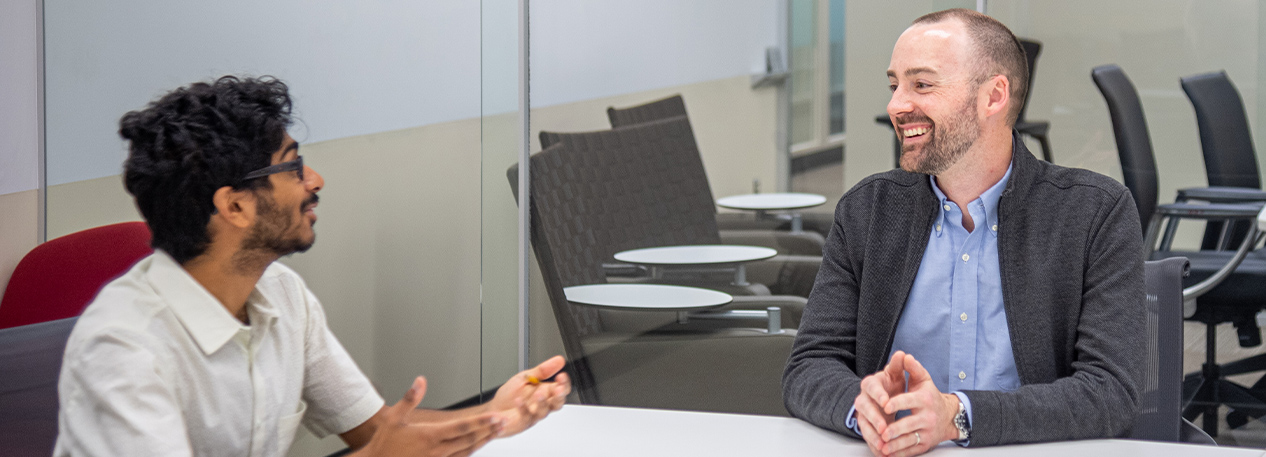 Economic advisor and economist Bryan Stuart sitting at a conference table, talking with a colleague.