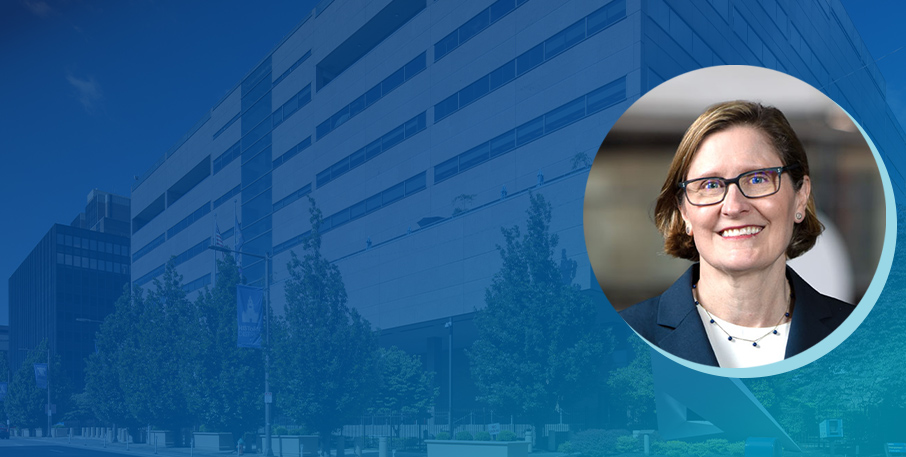 Photo of Anna Paulson in front of an image of the Federal Reserve Bank of Philadelphia building.