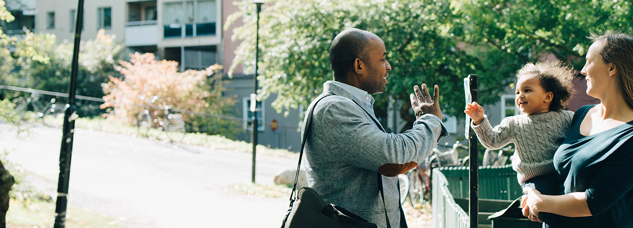 A father drops his child off at day care, and they wave goodbye to one another.